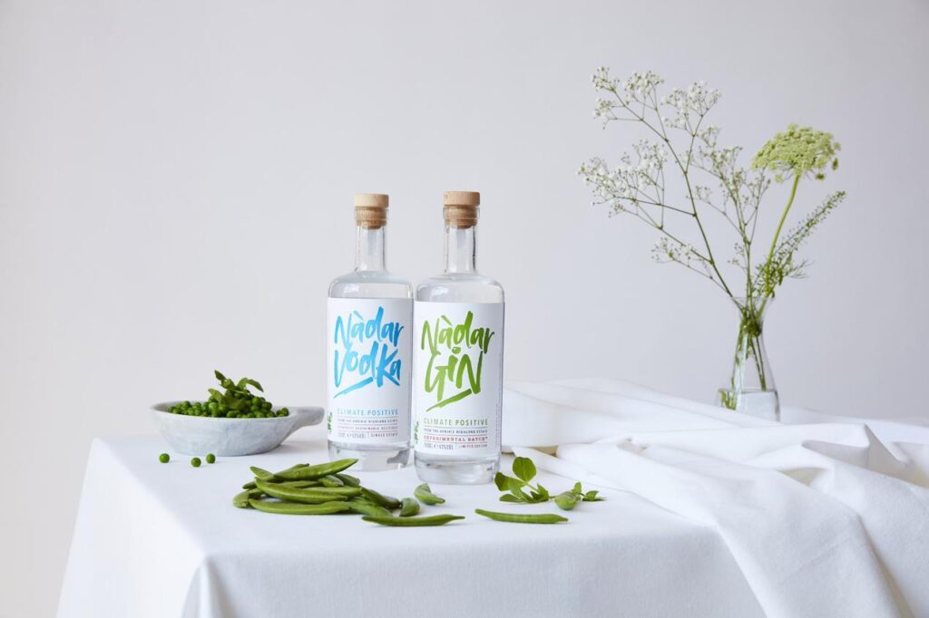 Bottle of vodka and bottle of gin on a table with a bowl of peas and vase of flowers. The vodka and gin was made by Arbikie Highland Estate.