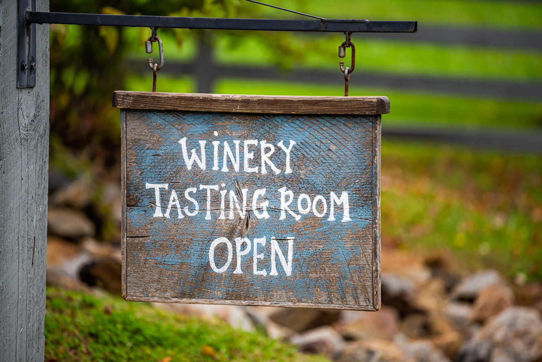 sign saying 'winery tasting room open' with a farm gate in the background