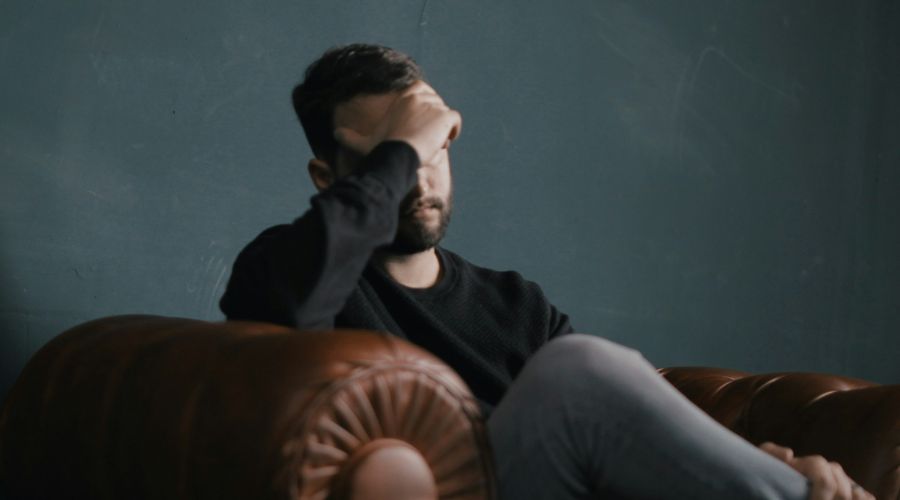 Man sitting on sofa alone with head in hands suffering with his mental health