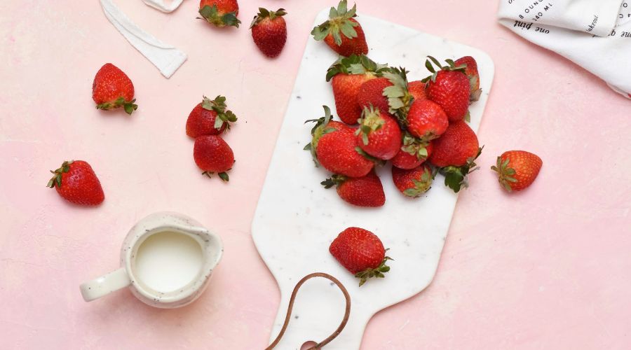 Strawberries on a chopping board with a jug of cream