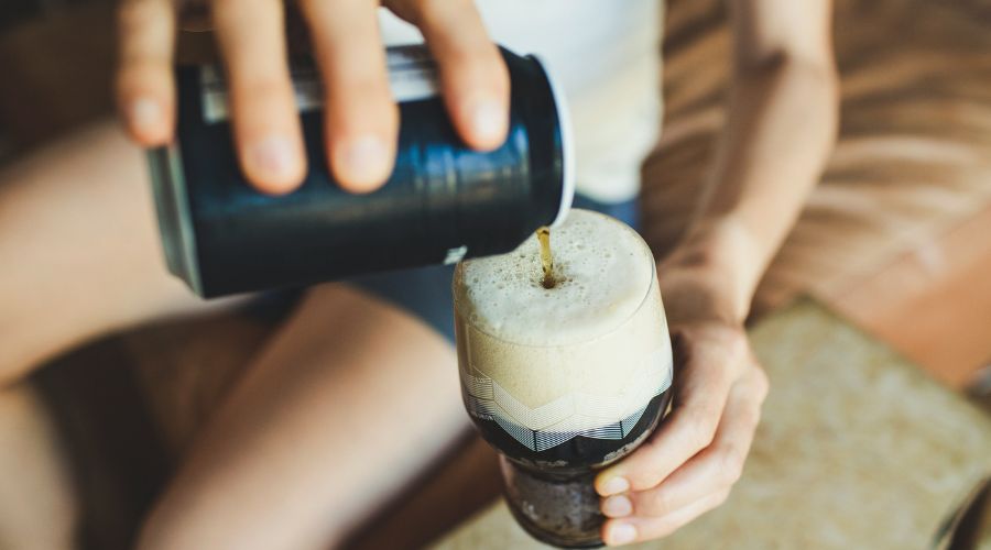 Stout drink being poured into glass by man in shorts